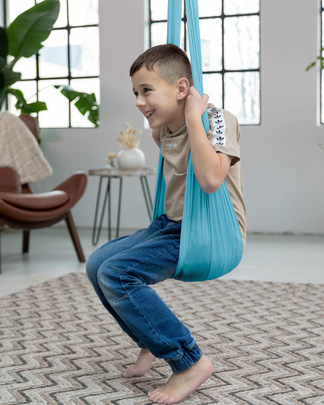Junge sitzt lachend in einer blauen Therapieschaukel aus Nylon – fördert Gleichgewicht und Körperwahrnehmung im Spiel
