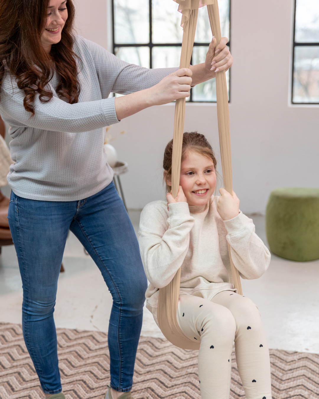 Mutter hilft ihrer Tochter in einem Schaukeltuch – spielerische Förderung von Gleichgewicht und Vertrauen mit Jolovi
