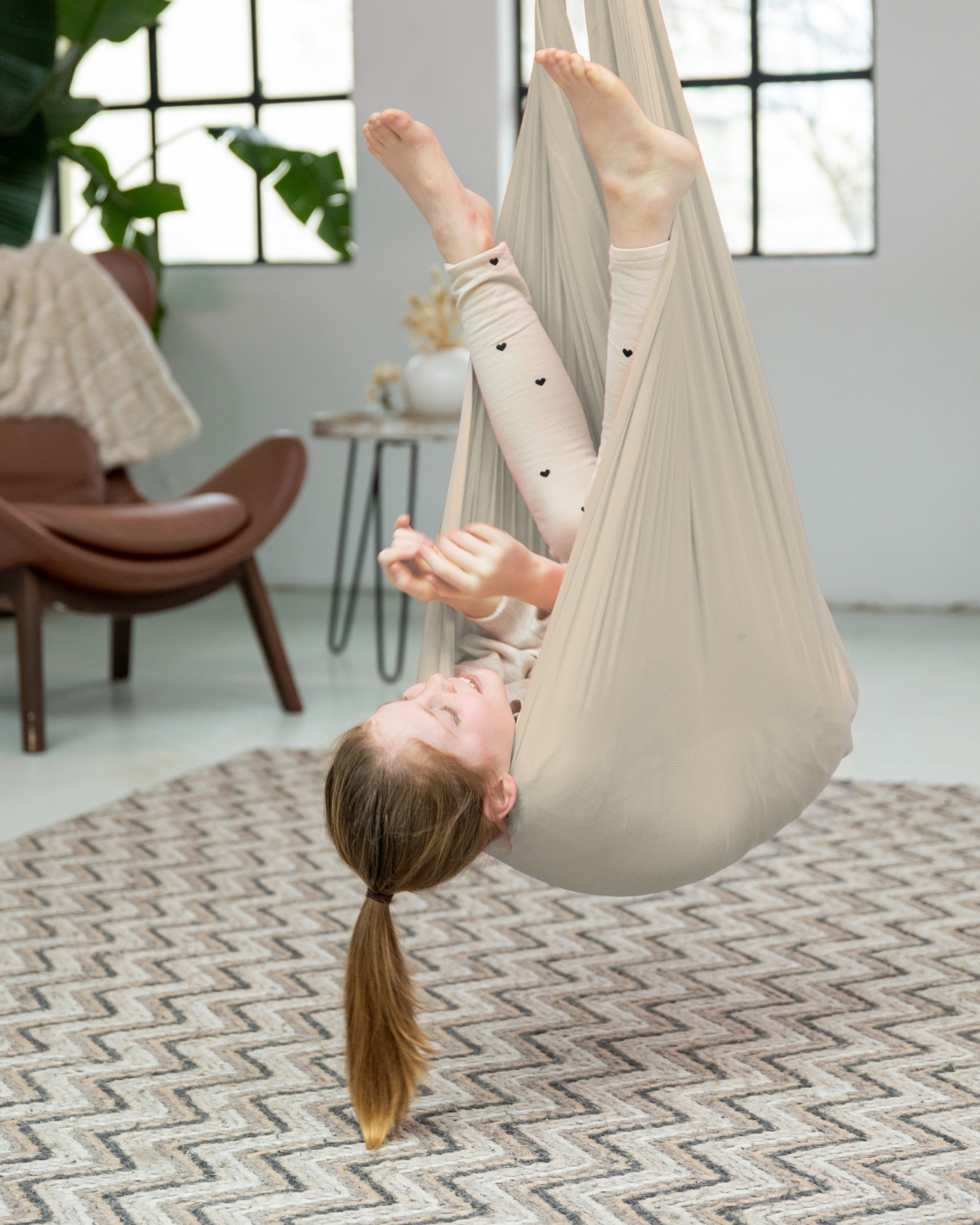Mädchen spielt kopfüber in beiger Therapieschaukel aus Nylon von Jolovi – ideal für Bewegungsförderung und Spielspaß im Kinderzimmer