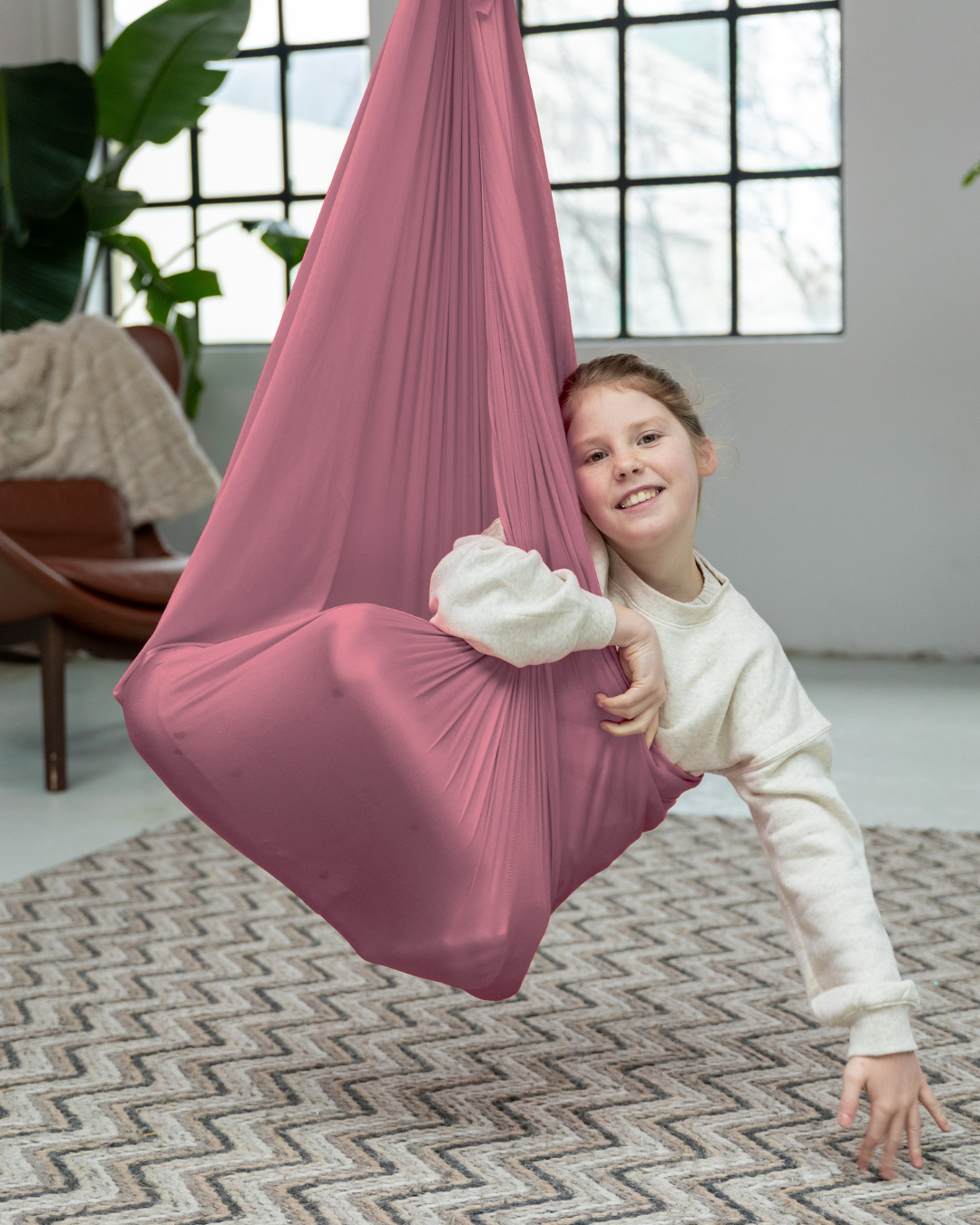 Mädchen spielt in rosa Therapieschaukel aus Nylon von Jolovi im Kinderzimmer – fördert Körperwahrnehmung und Entspannung