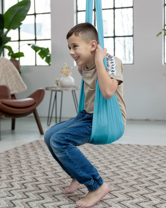Junge sitzt lachend in einer blauen Therapieschaukel aus Nylon – fördert Gleichgewicht und Körperwahrnehmung im Spiel