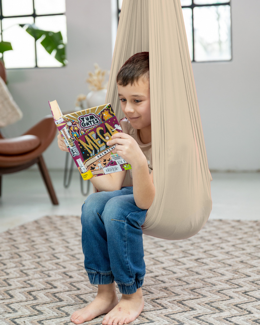 Junge liest entspannt in beiger Therapieschaukel aus Nylon von Jolovi – ideale Leseecke fürs Kinderzimmer